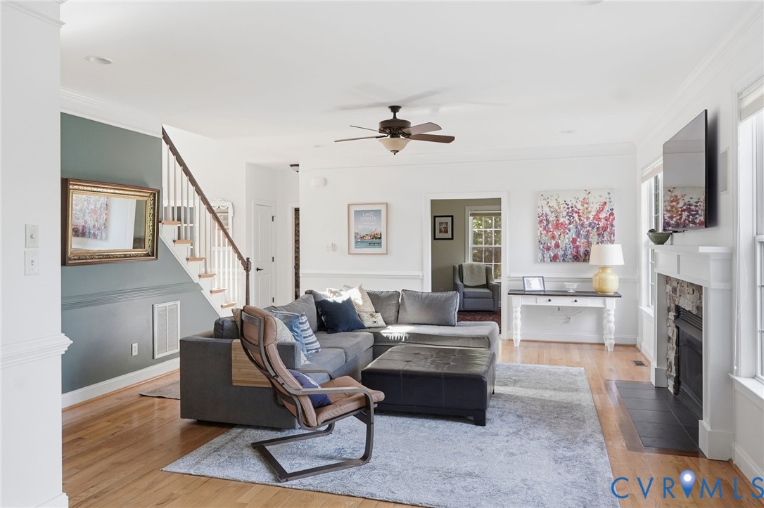 Living area featuring wood-finish flooring, a stone-surround fireplace with a classic mantel, and a ceiling fan