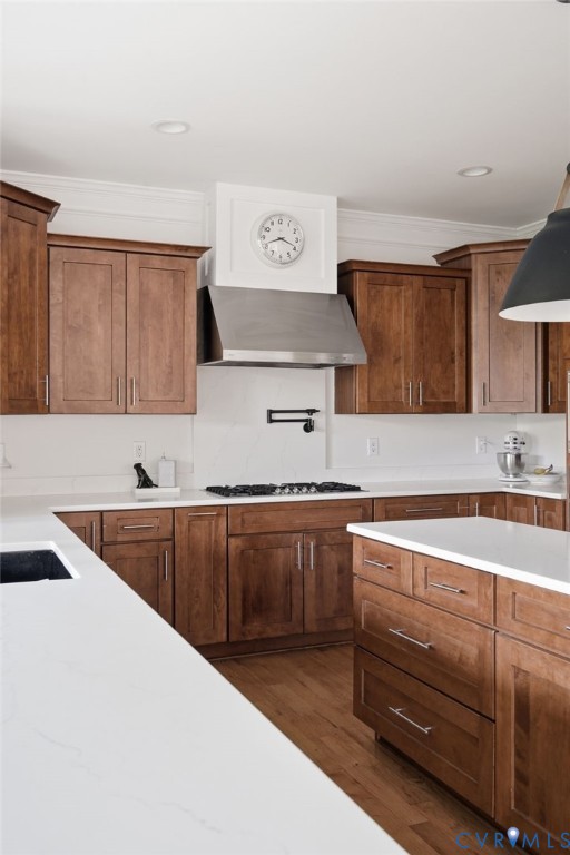 Kitchen featuring wood cabinetry, white stone-finish countertops, stainless steel range hood, wall-mounted pot filler, and wood-finish flooring