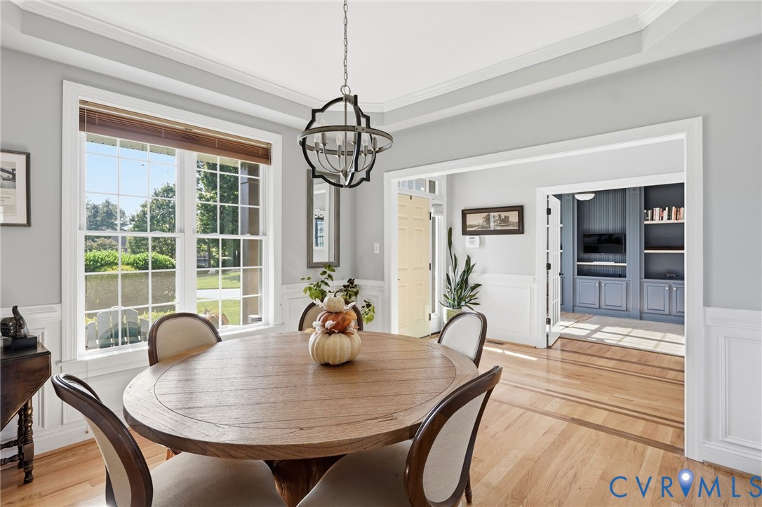 Dining space featuring tray ceilings, wainscoting, decorative metal chandelier, and wood-finish flooring