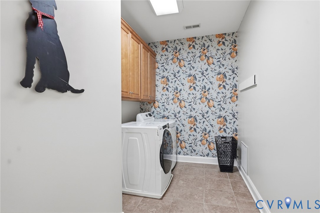 Utility space featuring patterned wall covering, wood-finish upper cabinetry, and ceramic tile flooring