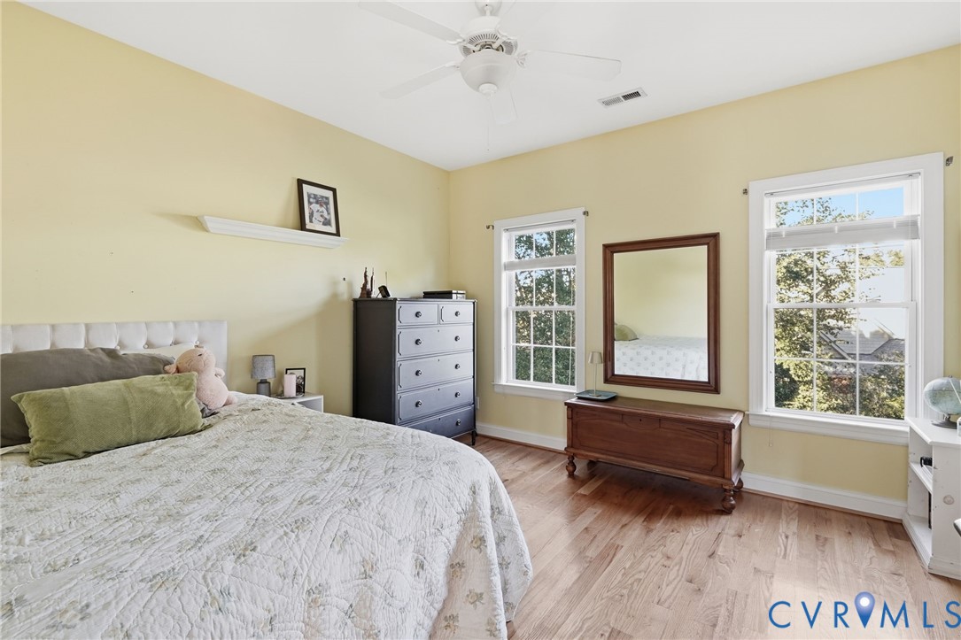 Room featuring wood-finish flooring, two double-hung windows with white casings, a ceiling-mounted fan, and a built-in wall shelf