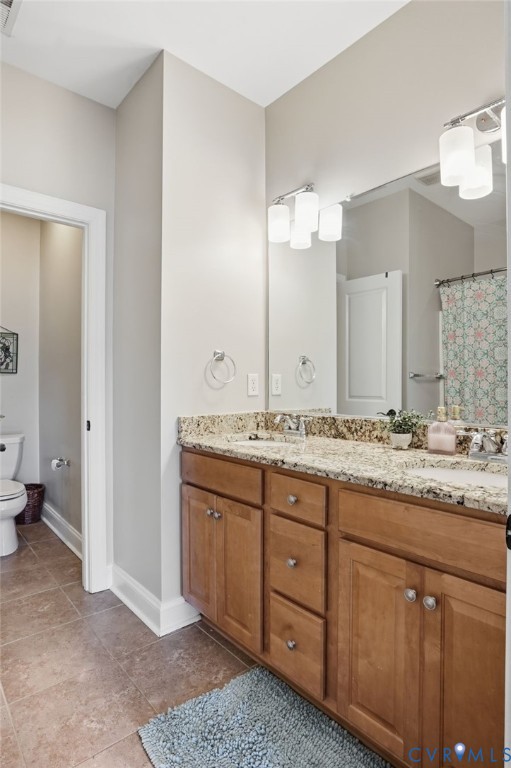 Bathroom featuring a dual-sink vanity with stone-finish countertops, wood-finish cabinetry, a large wall-mounted mirror, and ceramic tile flooring