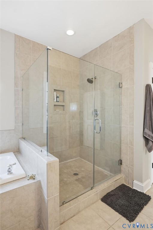 Glass-enclosed shower with a polished chrome showerhead, integrated tiled wall niches, tile surround, and adjacent built-in soaking tub