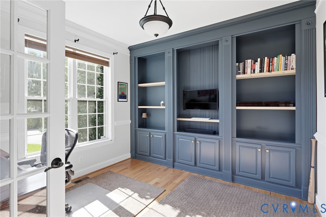 Built-in floor-to-ceiling cabinetry with decorative fluting, wood-finish flooring, multi-pane glass French doors, and an overhead semi-flush mount light fixture Built-in floor-to-ceiling cabinetry with decorative fluting, wood-finish flooring, multi-pane glass French doors, and an overhead semi-flush mount light fixture