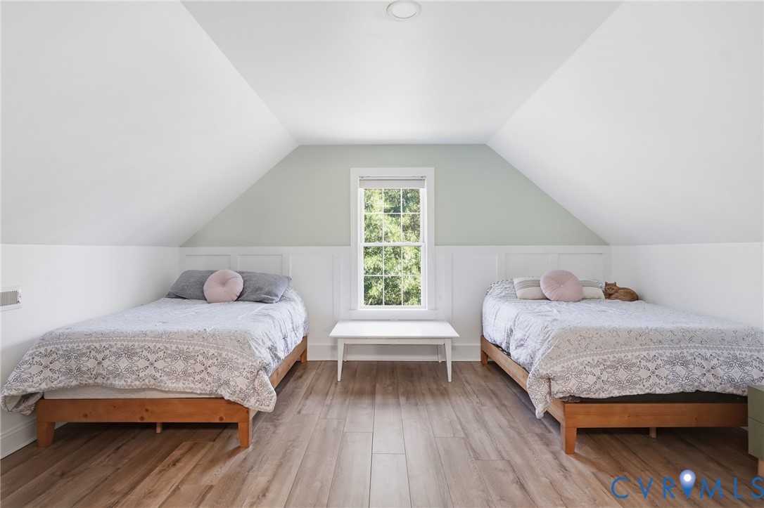 Vaulted ceilings with crisp white finish, integrated wood-finish flooring, half-wall wainscoting, and a central double-hung window