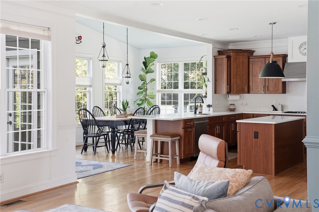 Kitchen featuring medium-toned wood cabinetry, stone countertops, a center island with a stone top, wood-finish flooring, and multi-pane windows Kitchen featuring medium-toned wood cabinetry, stone countertops, a center island with a stone top, wood-finish flooring, and multi-pane windows