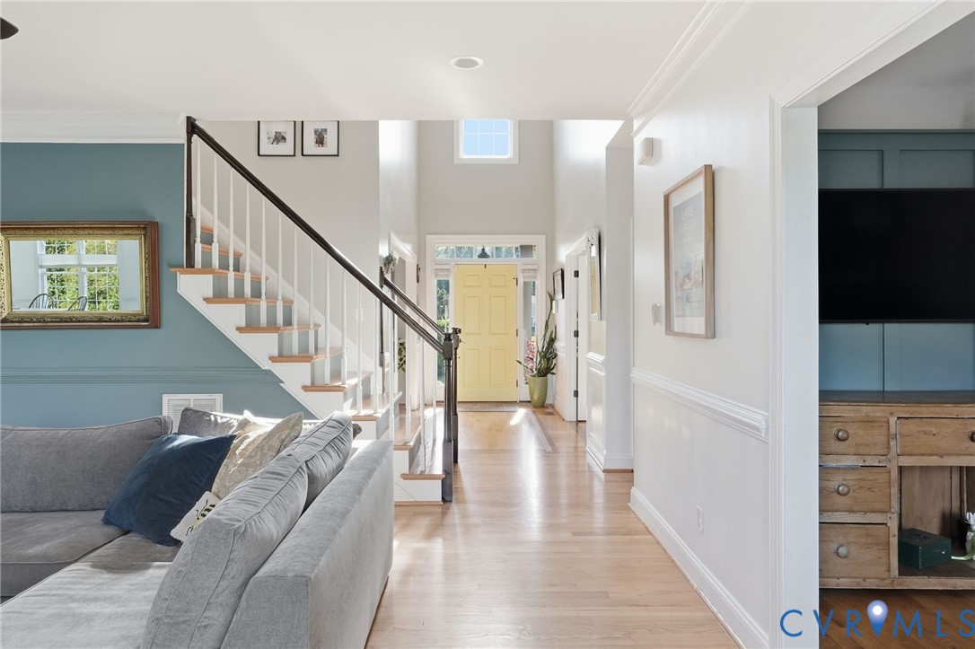Foyer featuring wood-finish flooring, a staircase with a dark wood handrail, high ceilings with a transom window, and paneled wainscoting