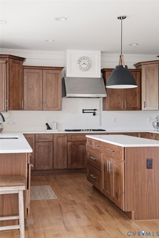 Kitchen featuring stained wood cabinetry, white countertops, stainless steel range hood, matte black pot filler faucet, and pendant lighting