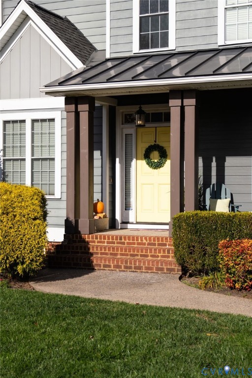 Covered front porch featuring brick steps, metal roofing, square columns, and a paneled entry door with a sidelight
