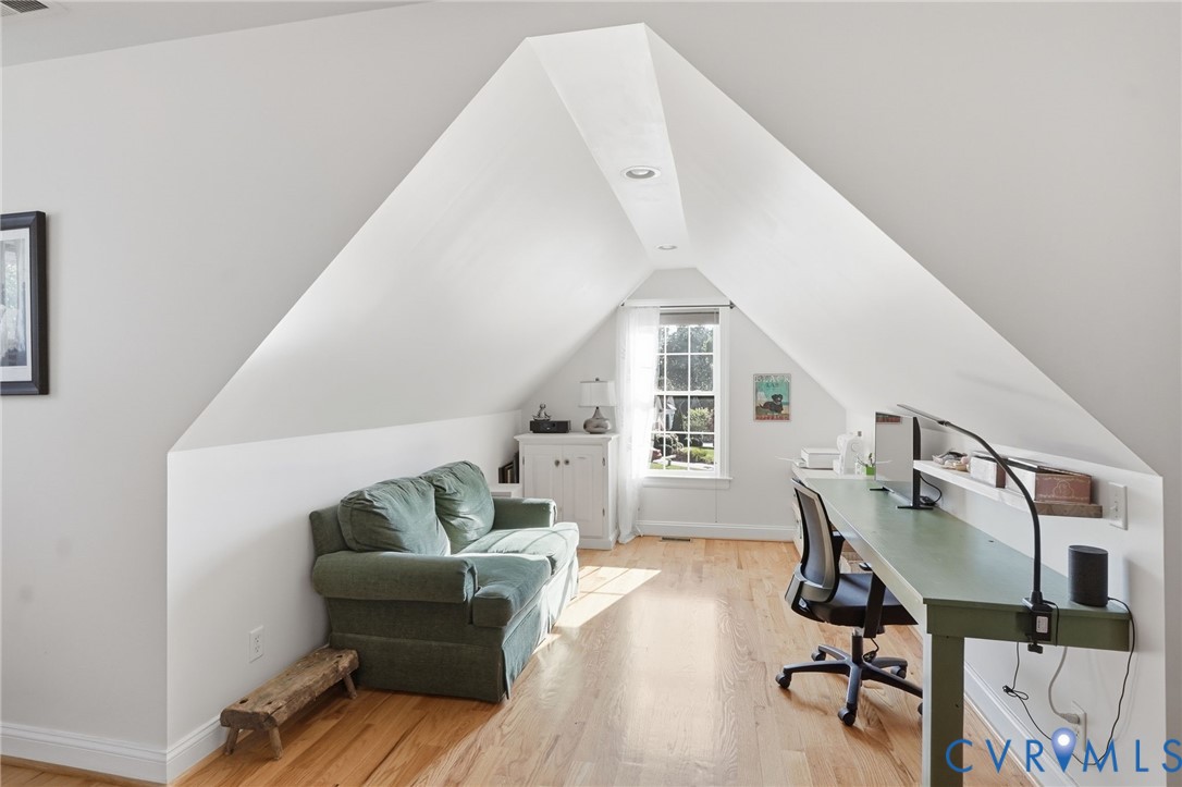 Vaulted ceiling with recessed lighting, wood-finish flooring, and a multi-pane window
