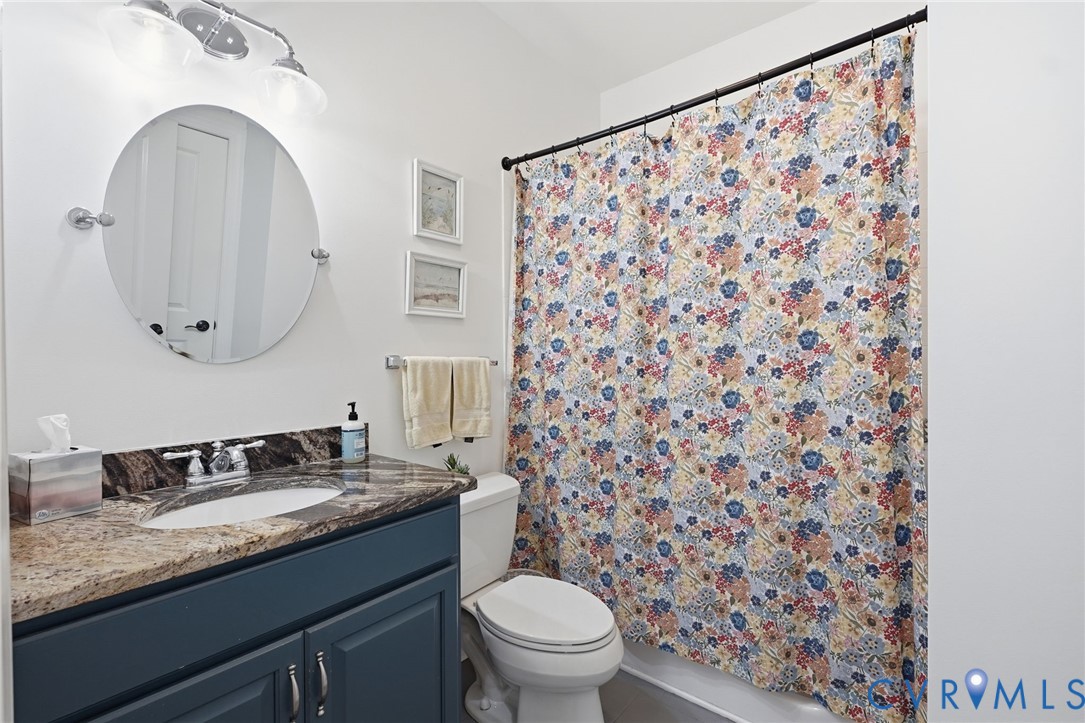 Blue-toned vanity cabinet featuring a stone-look countertop, integrated oval sink, circular wall-mounted mirror, and three-light overhead fixture