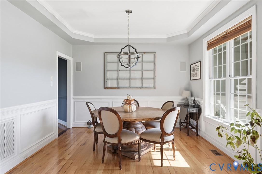 Dining space featuring wood-finish flooring, tray ceiling, wainscoting, multi-pane windows, and a metal orb chandelier Dining space featuring wood-finish flooring, tray ceiling, wainscoting, multi-pane windows, and a metal orb chandelier
