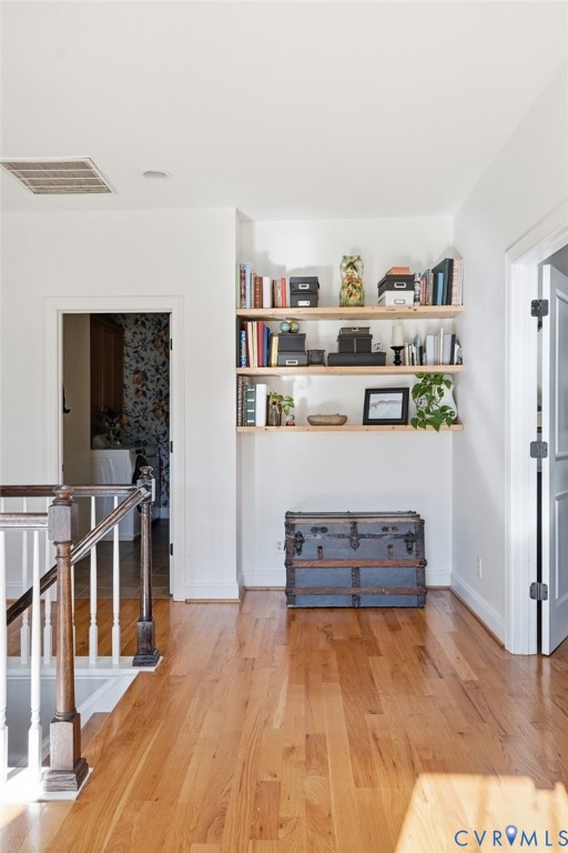 Built-in wall shelving, wood-finish flooring, and a staircase featuring a white balustrade with a contrasting stained-wood handrail