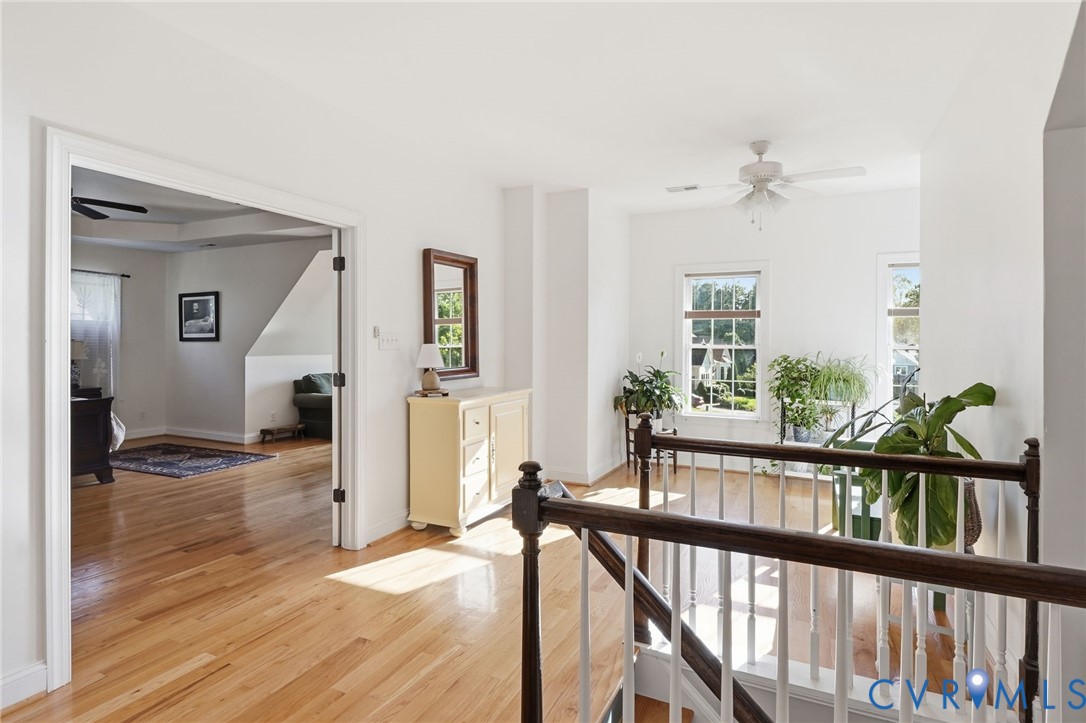 Landing area featuring wood-finish flooring, multi-pane windows, and a staircase with a white balustrade and dark wood handrail