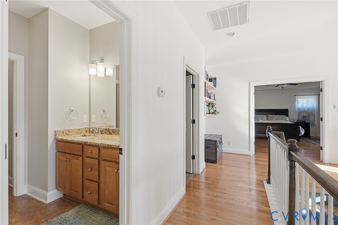 Bathroom vanity featuring stone-finish countertop, undermount sink, and wood cabinetry, complemented by wood-finish flooring and a staircase with a wooden handrail