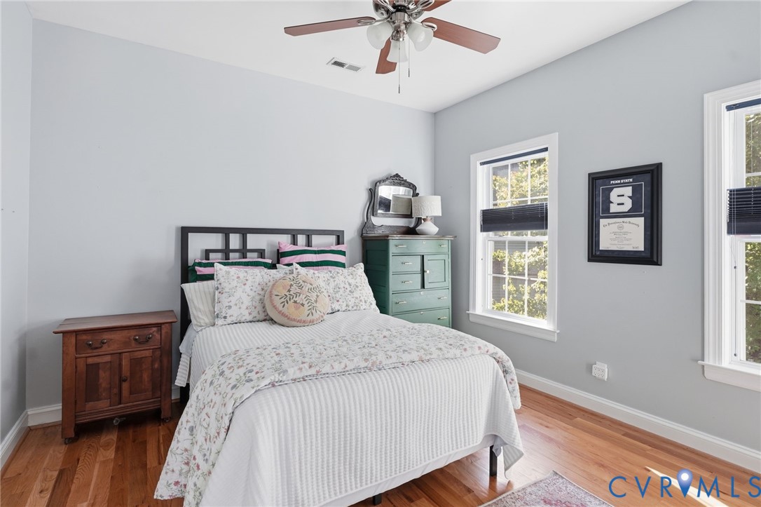 Neutral-toned room featuring wood-finish flooring, two windows with adjustable shades, and a ceiling-mounted fan with integrated lighting