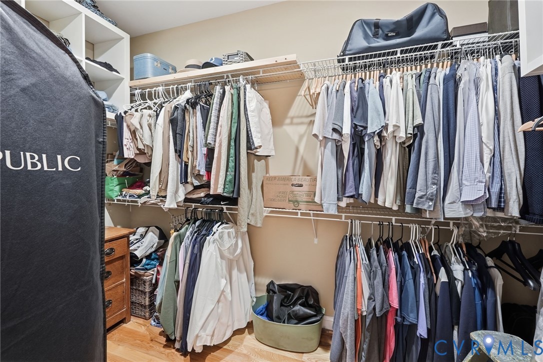 Walk-in closet featuring floor-to-ceiling built-in white shelving, wire rack hanging systems, and wood-finish flooring