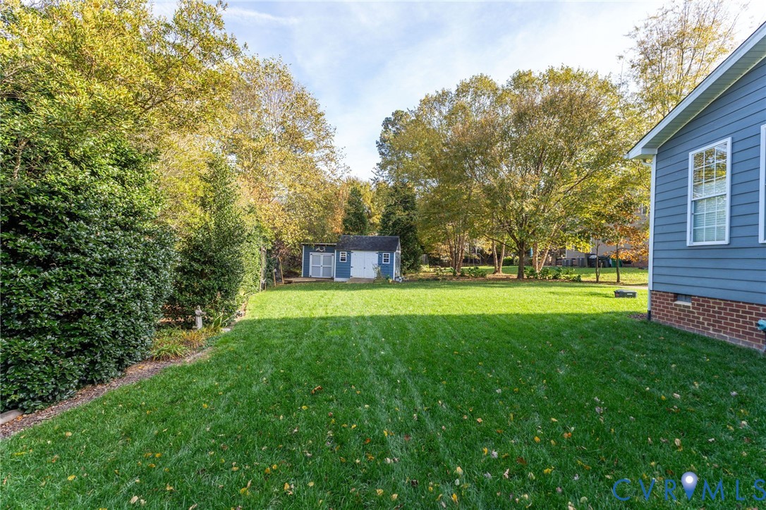 Expansive backyard featuring a level lawn, mature trees, a detached storage building, and horizontal lap siding with a brick foundation