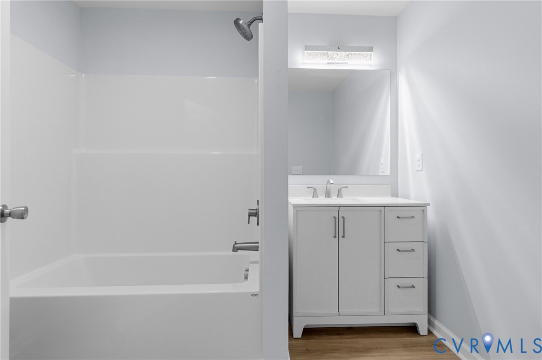 Bathroom featuring a white vanity with drawers, a rectangular mirror with integrated lighting, a tub-shower combination, and wood-finish flooring