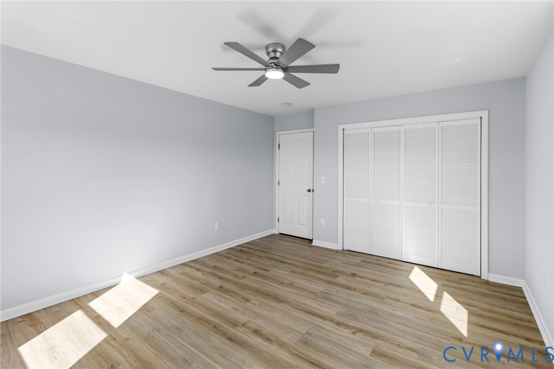 Neutral-toned walls, wood-finish flooring, ceiling fan with integrated light, and a double-door closet with louvered panels