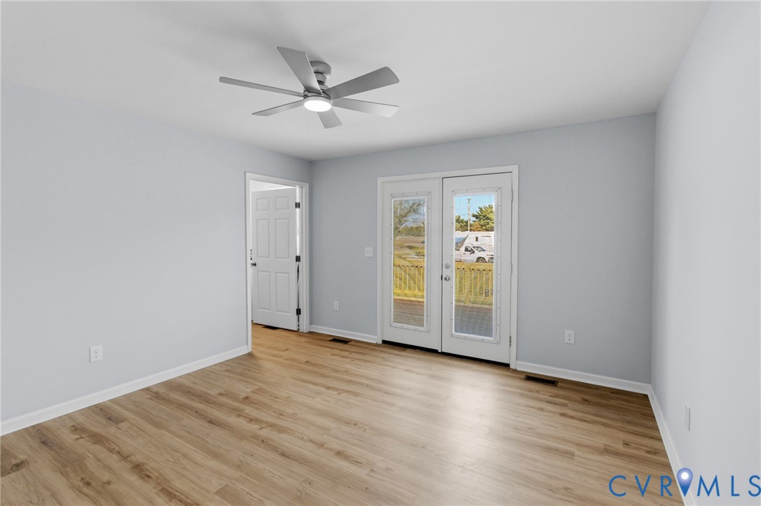 Interior space featuring wood-finish flooring, a multi-pane glass door, a neutral color palette, and a multi-blade ceiling fan with integrated lighting