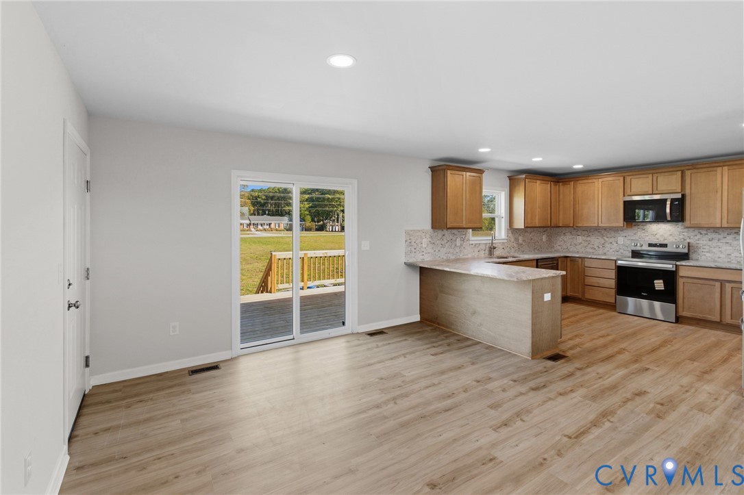 Kitchen featuring wood-finish cabinetry, stone-look countertops, stainless steel appliances, sliding glass doors, and light wood-finish flooring