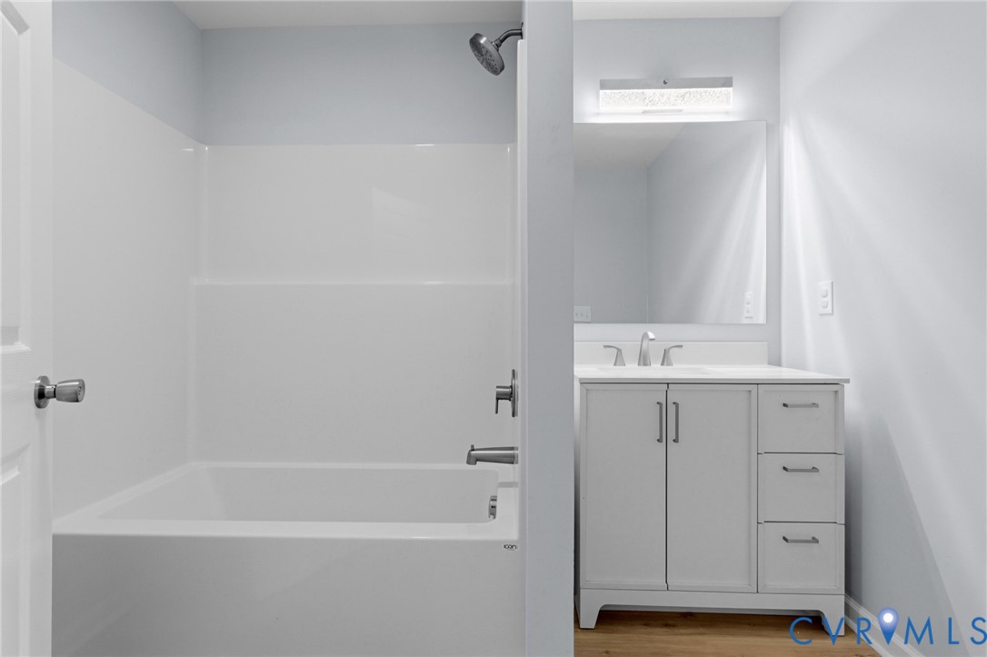 Bathroom featuring a white vanity with drawers, a rectangular mirror with integrated light fixture, and a tub-shower combination with a showerhead and metal faucet