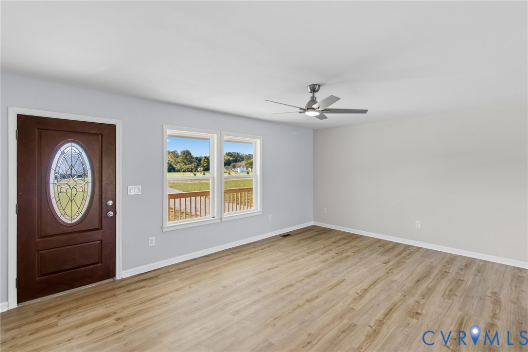 Wood-finish flooring, neutral wall tones, multi-pane entry door with oval decorative glass insert, dual windows with exterior rail visibility, and ceiling-mounted fan with integrated lighting
