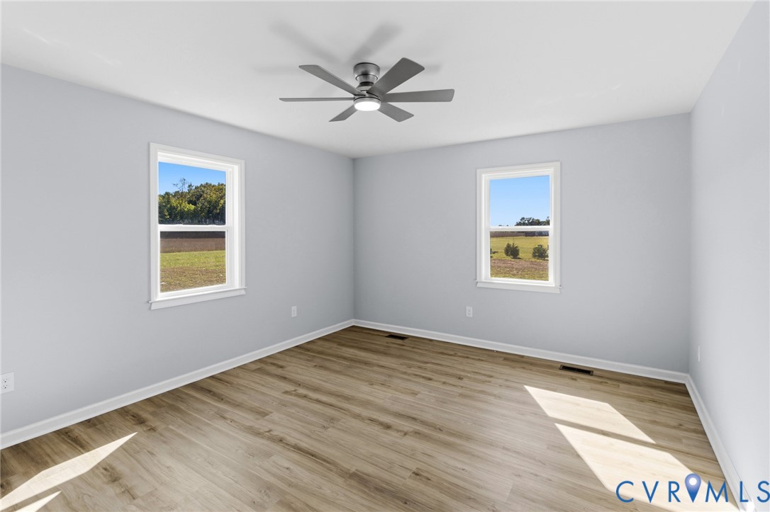 Room featuring wood-finish flooring, neutral wall paint, two dual-pane windows, and a central ceiling fan with integrated lighting