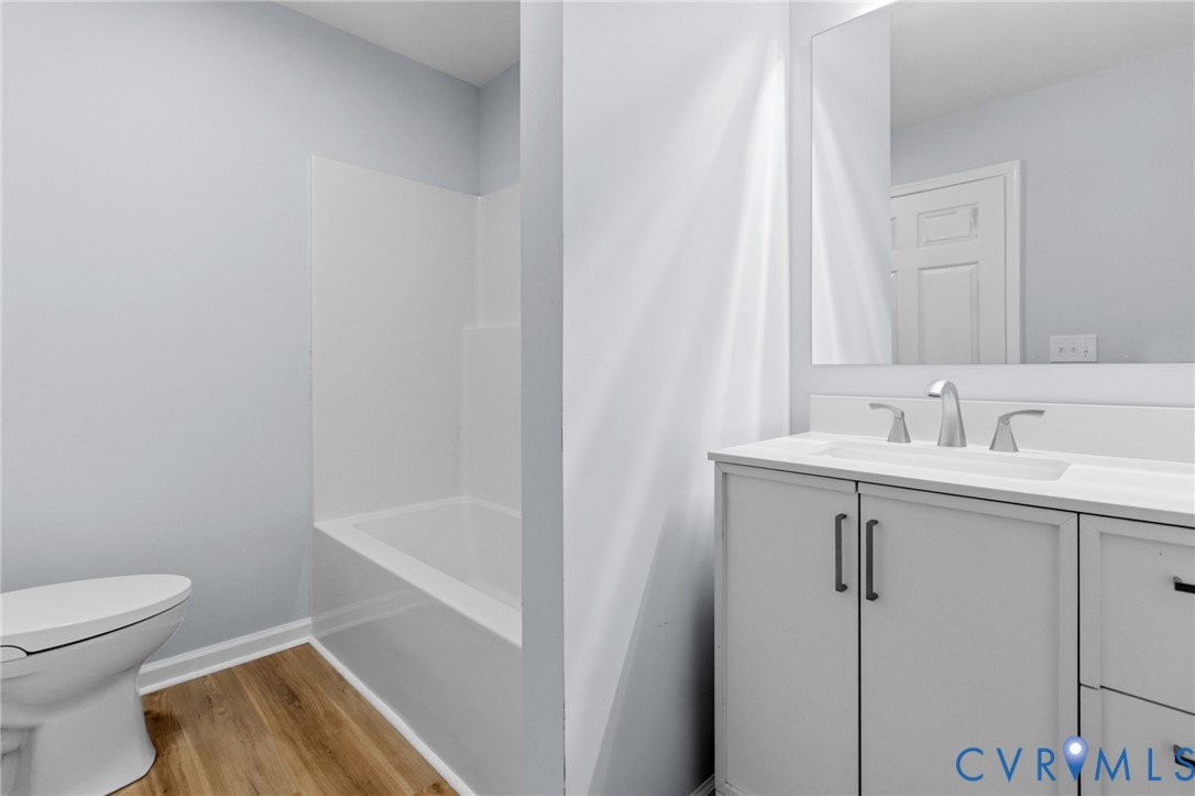 Bathroom featuring a white vanity with matte black hardware, integrated sink, large wall-mounted mirror, wood-finish flooring, and a shower-tub combination with a white surround