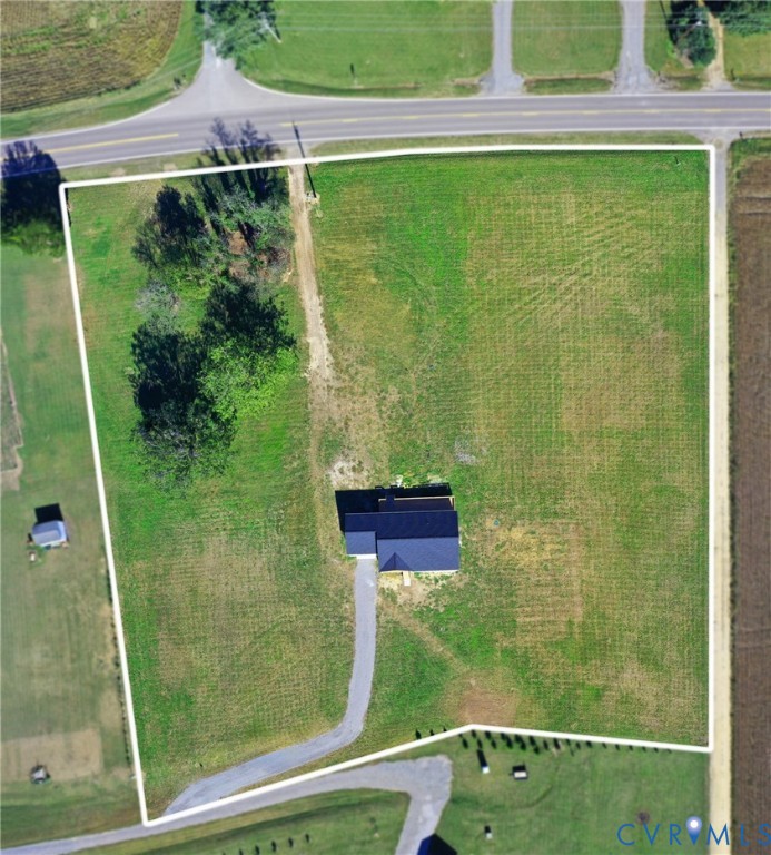 Aerial perspective of a sprawling lot featuring a paved driveway, extensive open acreage, and a collection of mature trees