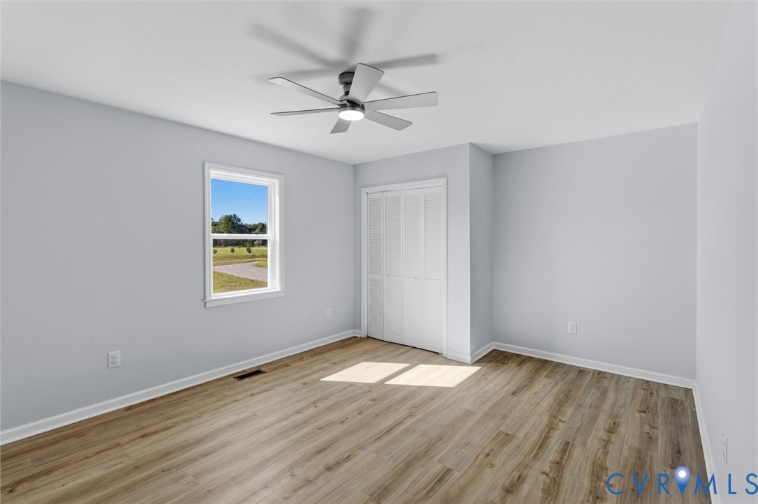 Interior room featuring wood-finish flooring, a multi-blade ceiling fan with integrated lighting, and a bifold closet door