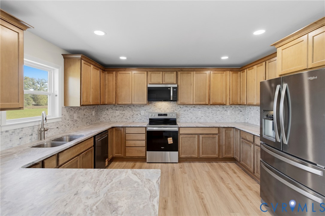 Kitchen featuring natural-finish wood cabinetry, stone-patterned countertops, mosaic tile backsplash, stainless steel appliances, and wood-finish flooring