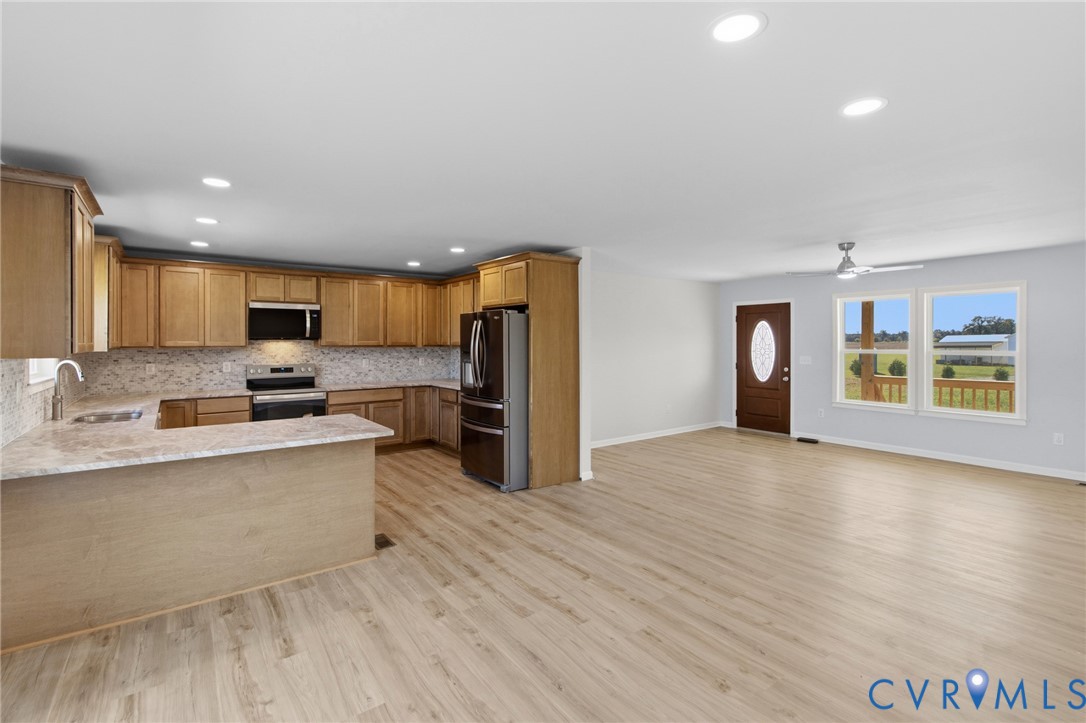 Open-concept interior featuring wood-finish flooring, recessed lighting, shaker-style wood cabinetry, stone-finish countertops, and stainless steel appliances