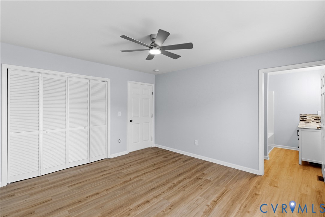 Interior room featuring wood-finish flooring, a multi-blade ceiling fan with integrated lighting, and louvered bi-fold closet doors