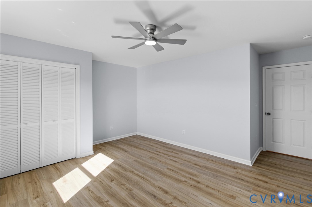 Interior space featuring wood-finish flooring, neutral wall paint, bi-fold closet doors, a six-panel interior door, and a multi-blade ceiling fan with integrated lighting