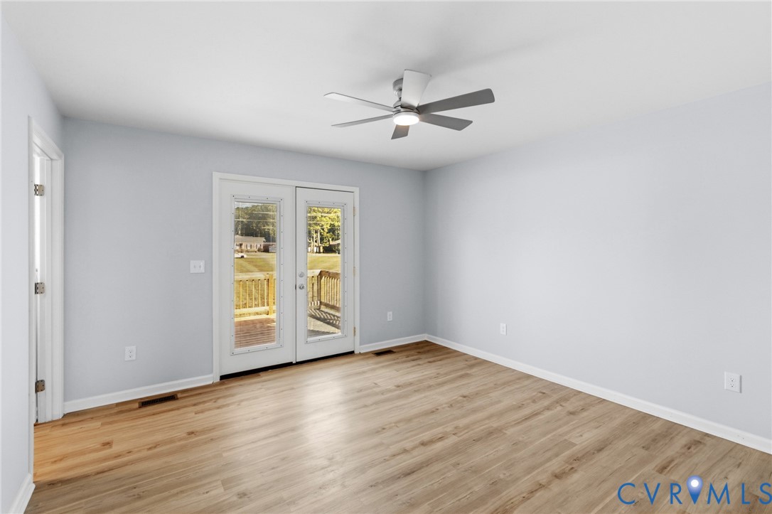 Neutral-toned room with wood-finish flooring, a multi-blade ceiling fan with integrated light, and glass-paneled double doors providing exterior access