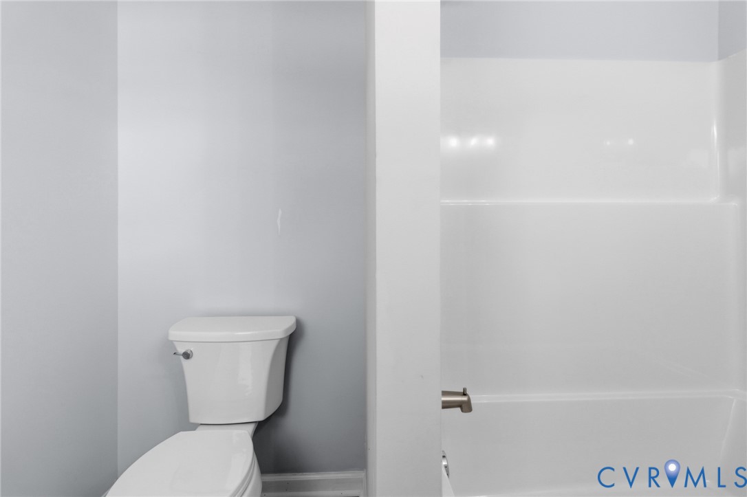 Full bathroom featuring a white porcelain toilet and a tub-shower combination with a white surround and metal faucet fixture