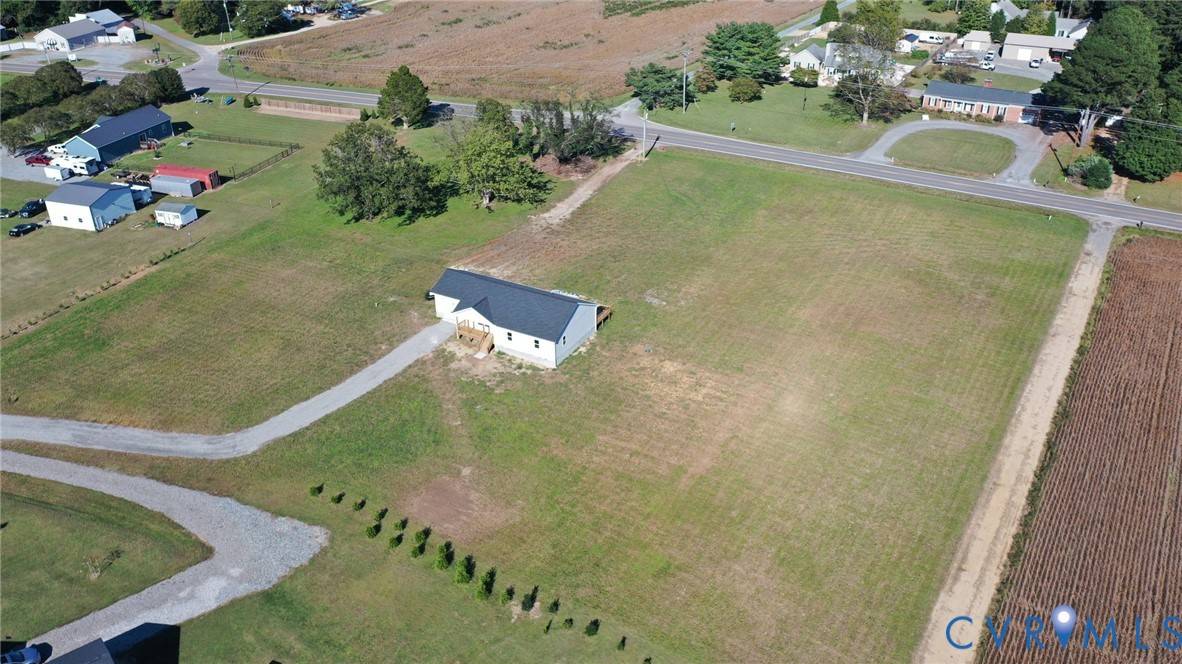 Single-story residence featuring a dark metal roof, expansive open acreage, and a long gravel driveway