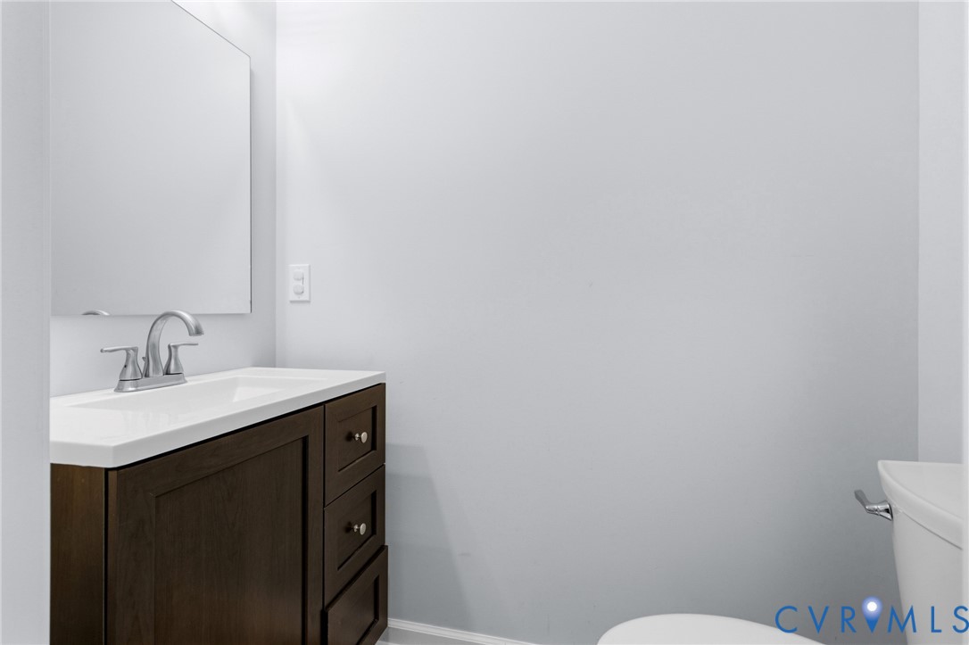 Dark-finish wood cabinetry, integrated rectangular vanity sink, polished chrome dual-handle faucet, large wall-mounted mirror, and a white toilet
