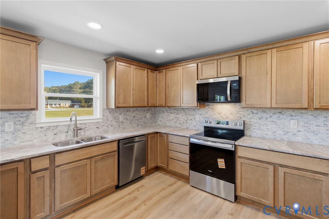 Kitchen featuring shaker-style light wood cabinetry, stone-patterned countertops, a mosaic tile backsplash, stainless steel appliances, and wood-finish flooring