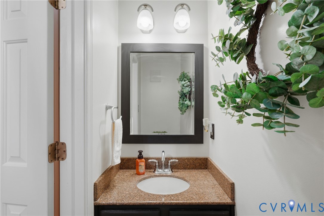 Vanity featuring a stone-composite countertop with an undermount sink, dark-finish cabinetry, a framed mirror, and dual wall-mounted light fixtures