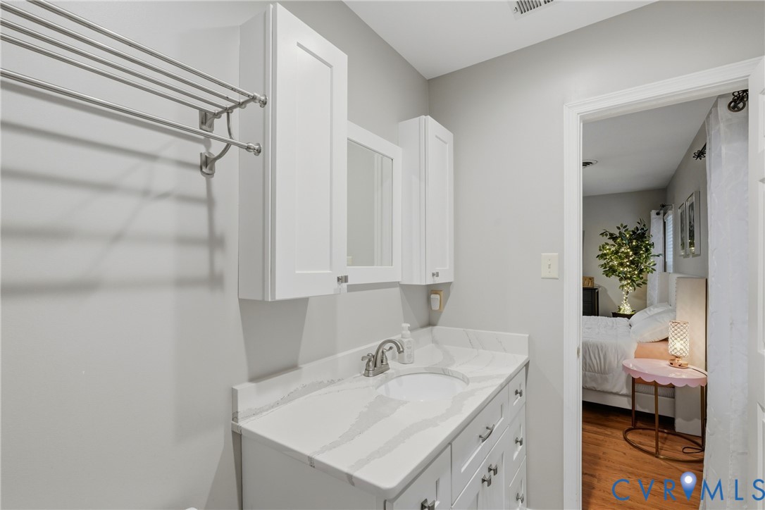 Bathroom featuring a white vanity cabinet with stone-patterned countertop, integrated undermount sink, wall-mounted storage cabinetry, and polished metal hardware