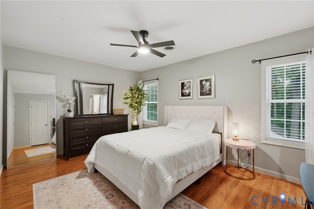 Wood-finish flooring, central ceiling fan with integrated lighting, neutral wall paint, and multi-pane windows with horizontal blinds
