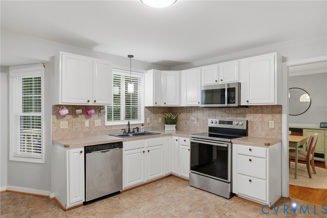 Kitchen featuring white cabinetry, stainless steel appliances, tiled backsplash, neutral-toned countertops, and tile flooring