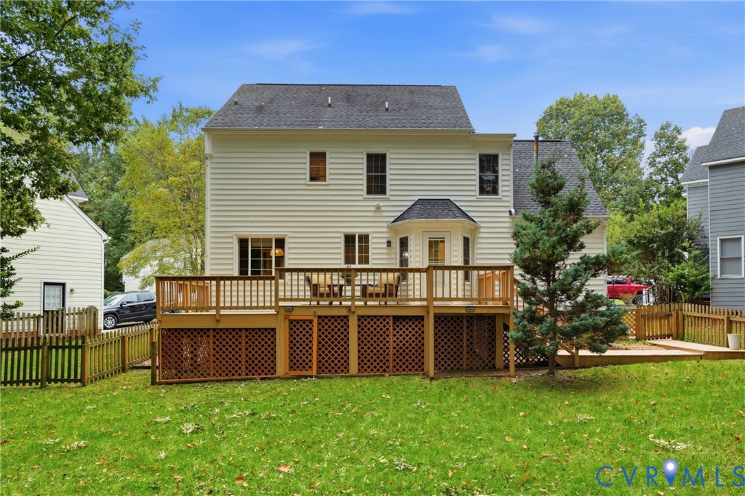 Rear elevation featuring light-colored horizontal siding, an elevated wood deck with lattice skirting, and a grassy backyard enclosed by wood fencing