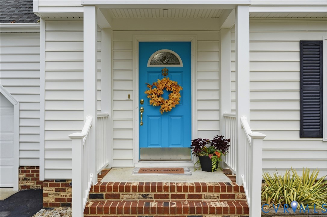 Front entrance featuring white lap siding, brick foundation detailing, a solid door with a semi-circular glass insert, and a covered porch with white railing