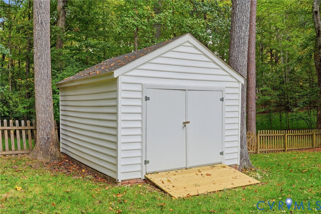 Freestanding outdoor storage shed featuring white horizontal siding, a gabled roof, double doors, and an integrated wooden ramp