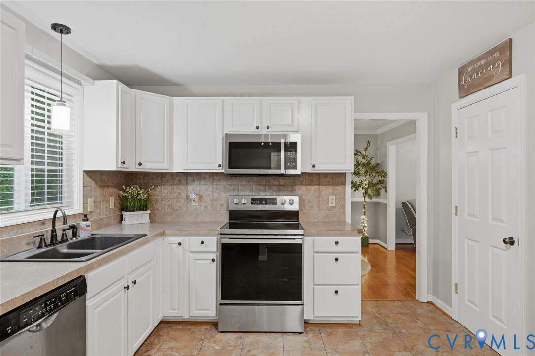 Kitchen featuring white shaker-style cabinetry, stainless steel appliances, ceramic tile backsplash, dual-basin sink with a gooseneck faucet, and tile flooring