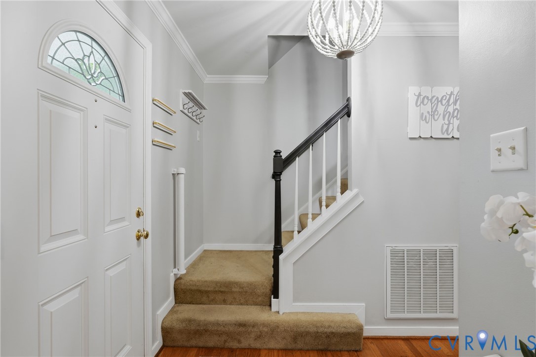 Foyer entrance featuring a front door with an arched glass transom, a decorative beaded light fixture, and a staircase with a dark-finished handrail and white balusters